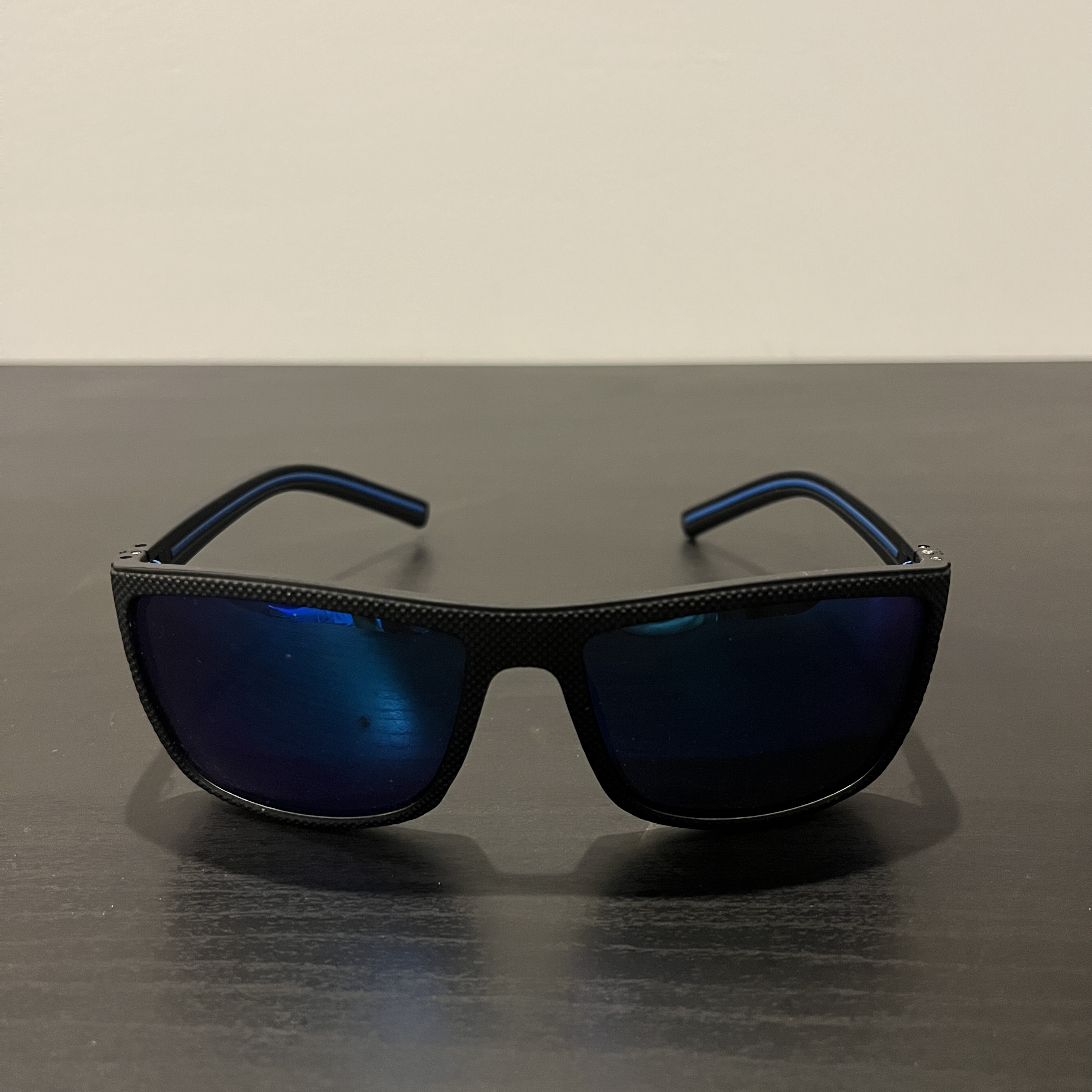 Black-rimmed sunglasses with blue lenses staged on a black table facing forwards.