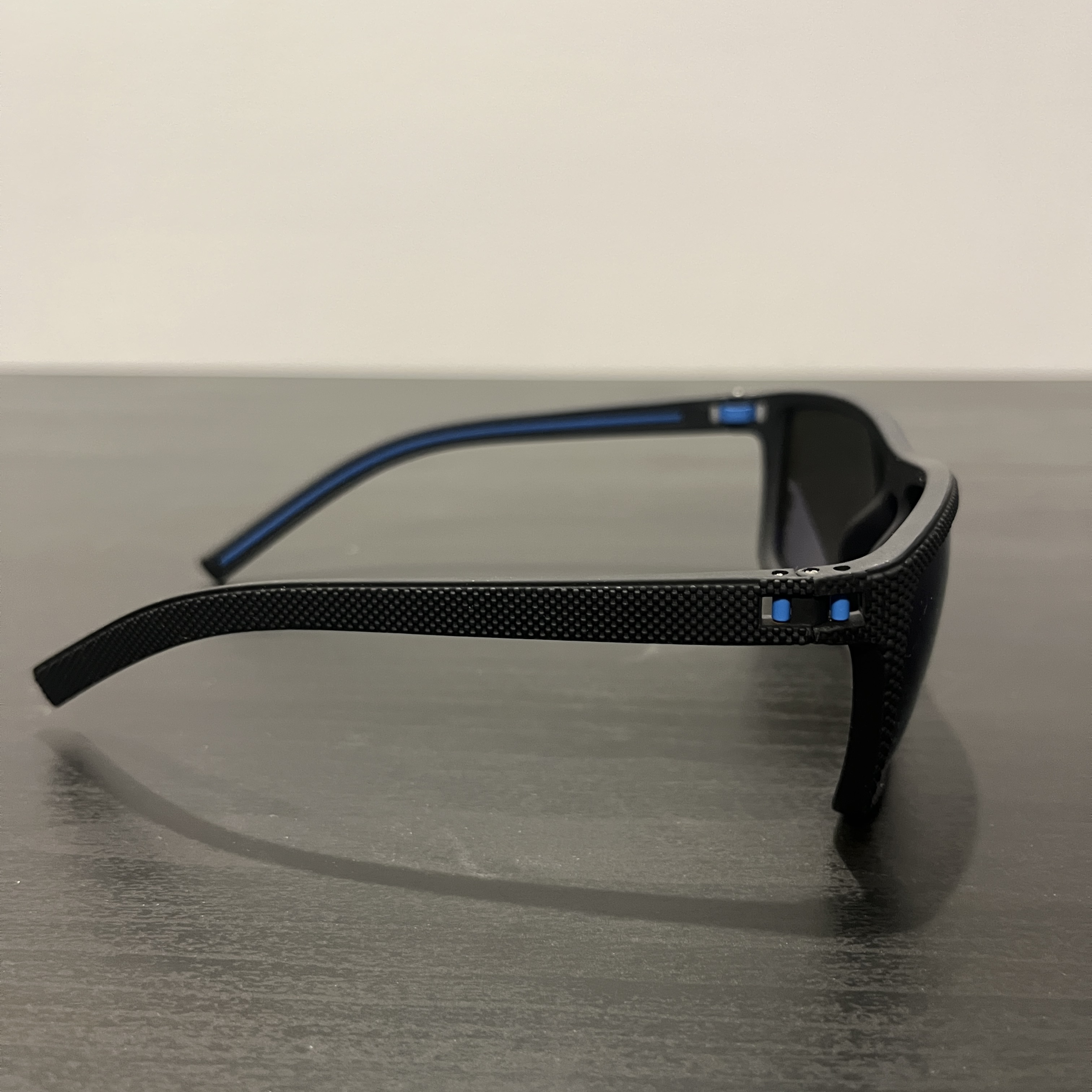 Black-rimmed sunglasses with blue lenses staged on a black table on its side.